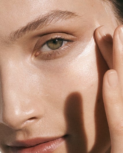 Model face applying cream to her face under the eye in an upwards motion with her index finger.